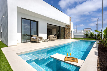 Luxury poolside patio with lounge chairs and drinks beside white villa under blue sky