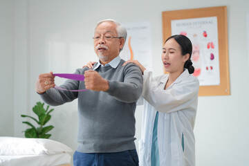 A caring physical therapist guides a senior Asian woman through resistance band exercises during a...