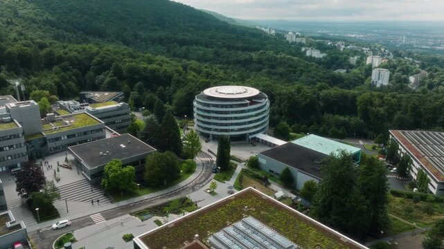 A drone performs a left-to-right panning movement while keeping the DKFZ round building centered, revealing green roofs, surrounding facilities and the forested hillside