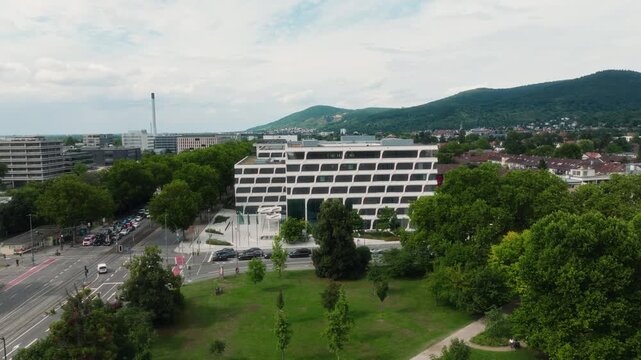 Circular lateral drone pan above park toward European Patent Office with tram and traffic.