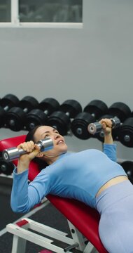 Close-up view of a middle aged fit Caucasian woman during gym workout. Bench press with dumbbells for chest. Gym scene shows woman performing bench press to tone chest and upper body.