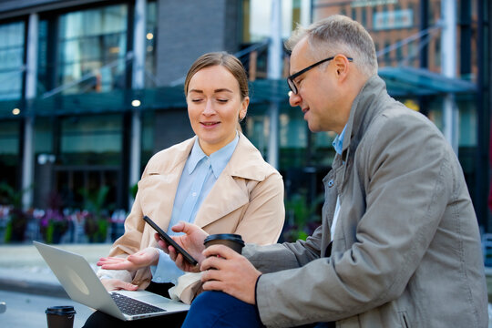 Professionals have outdoor business meeting using laptop and phones in urban environment. Networking and discussion.