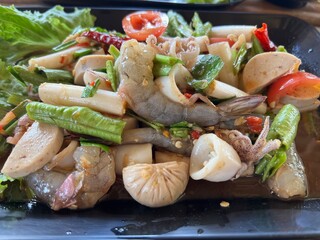 Table top view Thai spicy seafood salad on black plate.