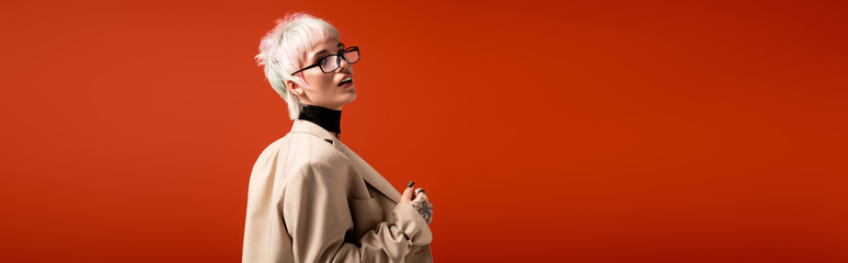 Young woman with stylish glasses poses against a vibrant orange backdrop, radiating confidence