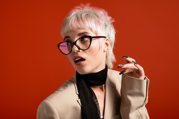Young woman with stylish hair and glasses poses against a vibrant backdrop with confidence