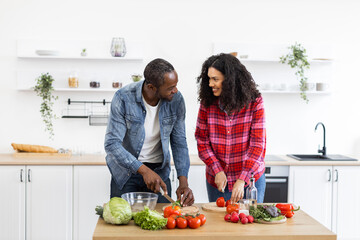 A smiling couple prepares a meal together in a bright, modern kitchen, chopping fresh vegetables.