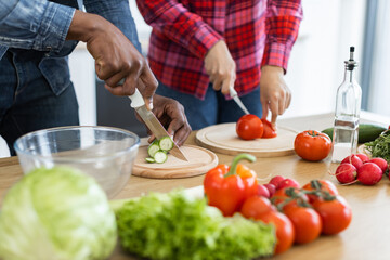 A couple prepares a healthy meal together, chopping fresh vegetables on a wooden countertop in a bright kitchen setting.
