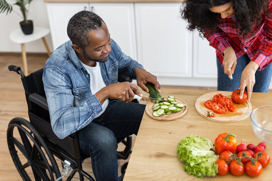 A diverse couple prepares a healthy meal together in a bright kitchen, one using a wheelchair.