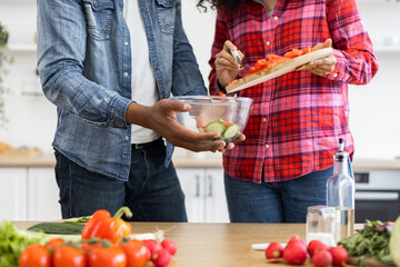 A couple is preparing a fresh salad in the kitchen, with various vegetables on the table.