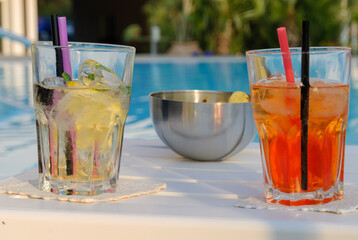 Two refreshing summer cocktails with ice by a poolside table, glowing in warm sunlight, creating a relaxed holiday and vacation vibe.