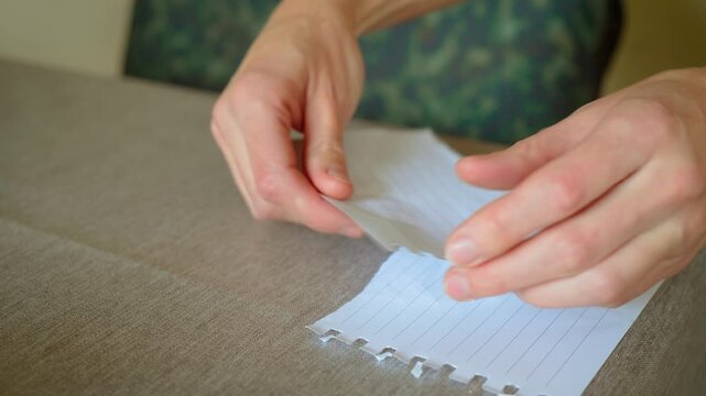 Tearing paper sheet into pieces reflecting psychological problems and depression. Ripping lined page into fragments symbolizing emotional struggle. Splitting notebook paper into torn bits conveying