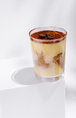 Tiramisu dessert in clear cup with cocoa and coffee beans on white background