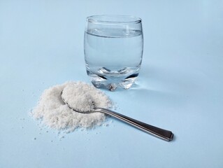 Salt water solution in glass and pile of salt with spoon on blue background 