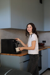 Woman preparing coffee with a home espresso machine in a modern kitchen, smiling during a relaxed morning routine