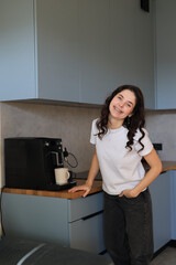 Smiling woman standing by an espresso machine in the kitchen, enjoying a light and cheerful moment at home