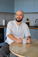 Man sitting at the kitchen table with a cup of coffee, looking to the side with a calm and thoughtful expression in a relaxed home environment