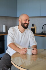 Smiling man enjoying a cup of coffee at the kitchen table, relaxed and cheerful morning moment at home