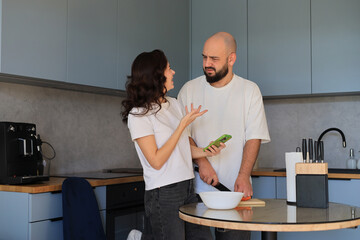 Couple having a playful discussion while preparing food in the kitchen, gesturing and interacting during a casual cooking moment