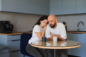 Couple sitting close together at the kitchen table, leaning on each other for emotional support during a quiet, thoughtful moment