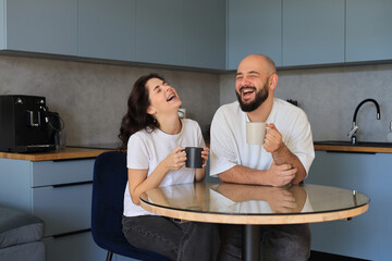 Couple laughing together at the kitchen table, sharing a lighthearted moment and enjoying each other&rsquo;s company
