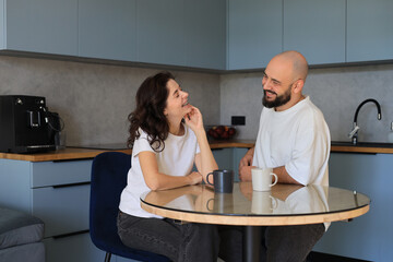 Couple smiling and talking at the kitchen table, enjoying a pleasant conversation and relaxed moment together in a cozy home environment