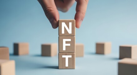 Hand placing nft wooden blocks on a blue background with other blocks scattered around in soft focus