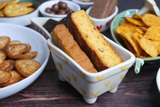 Assorted party snacks on table featuring chocolate cream sandwich biscuits, sugar coated heart cookies, wafer chocolates, chocolate coated caramel balls, salted crackers, and crispy potato chips.