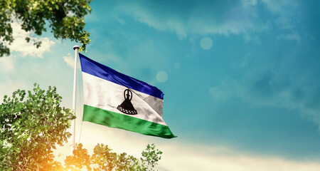 Lesotho national flag waving in the sky behind the tree. The flag blowing with beautiful sunlight. Lesotho national flag for independence day.