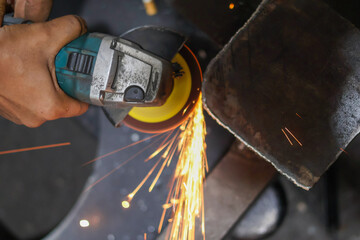 Overhead shot of an angle grinder operated by a worker, aggressively cutting metal and creating a...