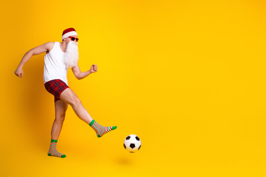 Santa Claus bearded man in pajama kicks soccer ball in bright yellow studio for festive holiday vibe