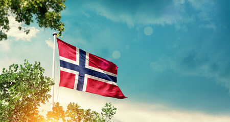 Norway national flag waving in the sky behind the tree. The flag blowing with beautiful sunlight....