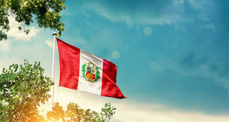 Peru national flag waving in the sky behind the tree. The flag blowing with beautiful sunlight. Peru national flag for independence day.