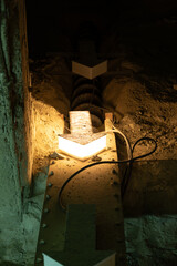 Close-up of an illuminated arrow guiding material flow into an obsolete Archimedes screw conveyor system in a dark, abandoned cement factory gallery.