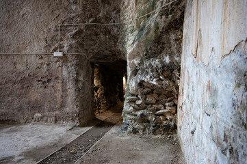 View of abandoned cement factory interior showing the narrow mine cart rails leading into a rough, dark tunnel entrance built into stone walls.