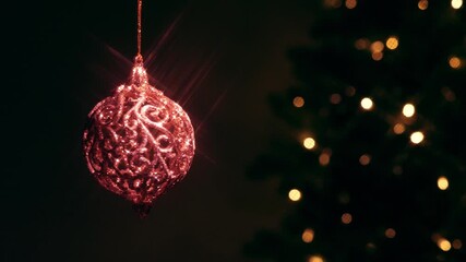 Sparkling ornate Christmas ornament hanging against a blurred background of a festive tree with warm bokeh lights, creating a cozy holiday atmosphere. - Powered by Adobe