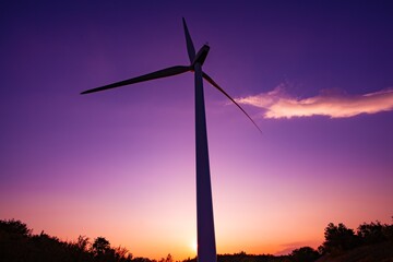 A Majestic Wind Turbine Silhouetted Against a Vibrant Sunset Sky, Showcasing Renewable Energy's Role in Sustainable Development and Nature's Beauty in Italy