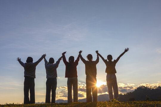 Successfully five friends holding raised hands standing on mountain at the sunset. Friendship holiday