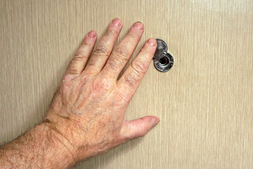 The hand of an elderly man opening or closing a door peephole. Security concept, monitoring neighbors.