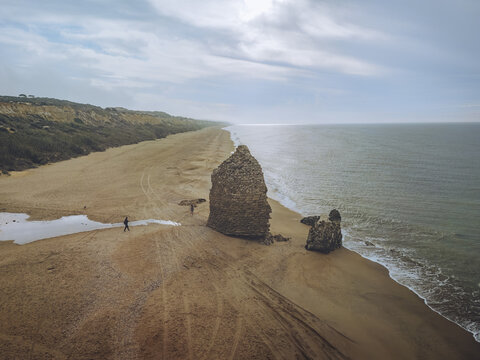 Aerial view of the rugged Torre del Loro coastline where golden sands meet the vast, turbulent sea under a moody sky, Mazagon, Andalusia, Spain.