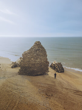 Aerial view of a solitary figure walking along the sandy shore near the weathered Torre del Loro cliffs, where the golden sand meets the blue sea, Mazagon, Andalusia, Spain.