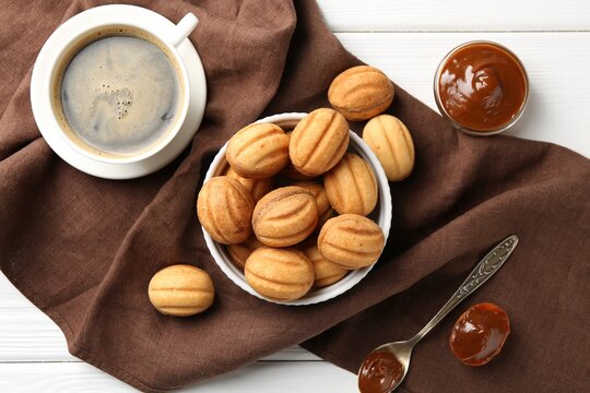 Delicious nut shaped cookies with boiled condensed milk served with coffee on white wooden table, flat lay