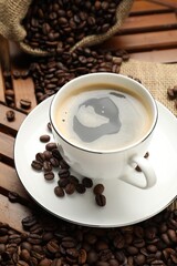 Aromatic coffee in cup and beans on wooden table, closeup