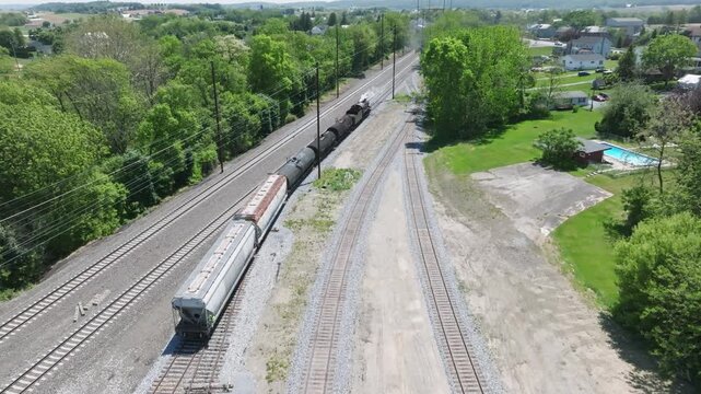 A vintage steam freight train makes its way backing up in yard performing switching operations moving steadily along the railway tracks in a peaceful countryside setting.