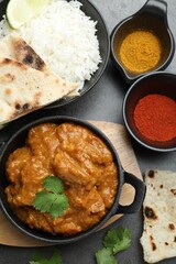 Delicious chicken tikka masala, rice, cilantro, lavash and spices on grey textured table, flat lay