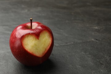 Red apple with carved heart on black table, closeup. Space for text