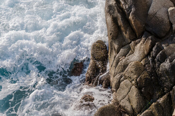 clear turquoise aegean sea water crashing the rocks close up. sea background with waves and foam. rocky coast with sea