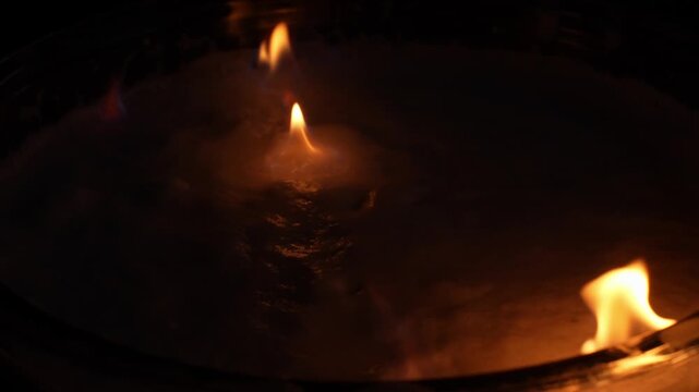 Flames dancing over a liquid surface within a glass container, creating a vibrant display of hot orange and yellow colors representing power, warmth, and intense energy, extreme close up, macro