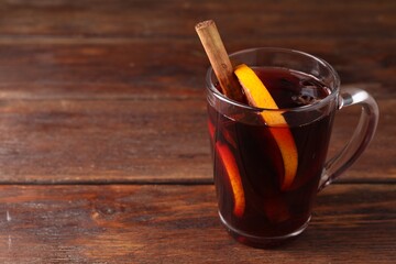 Tasty mulled wine with spices in glass cup on wooden table, closeup. Space for text