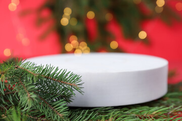 Empty podium and fir branches on red background against Christmas lights, selective focus