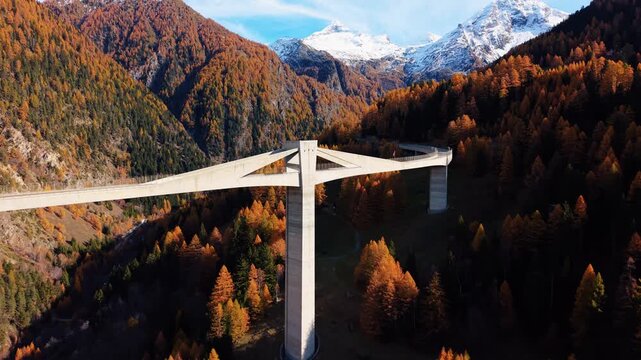 Aerial view of the majestic Ganter Bridge, a concrete structure amidst the colorful autumn trees and distant snow-capped mountains, Ried-Brig, Wallis, Switzerland.
